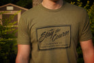 Person wearing a green t-shirt with 'Stay the Course Clothing Co' logo outdoors.