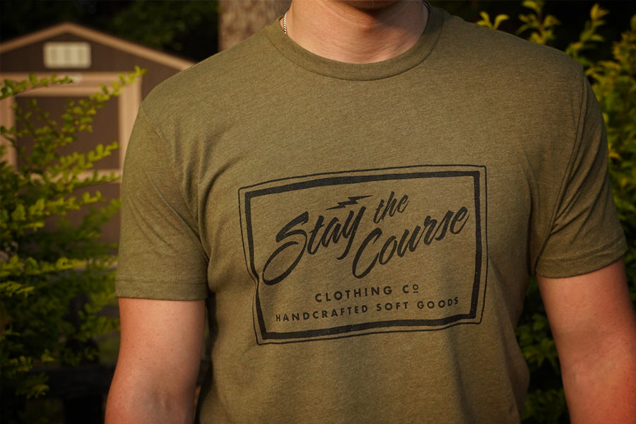 Person wearing a green t-shirt with 'Stay the Course Clothing Co' logo outdoors.