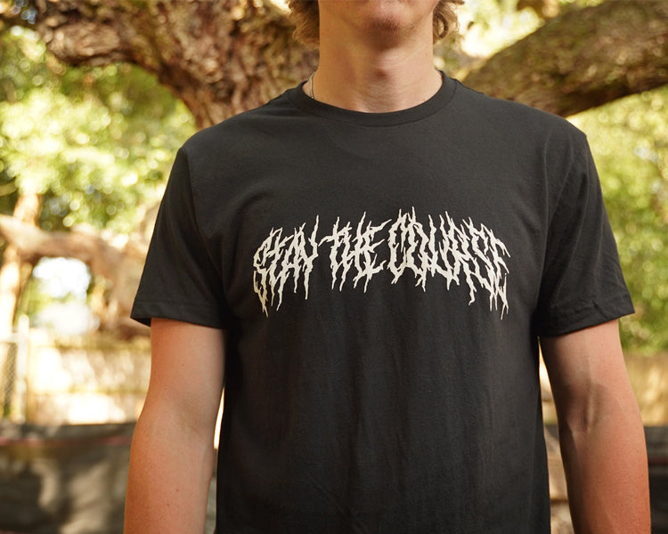 Person wearing a black T-shirt with "Stay the Course" printed in white in heavy metal style