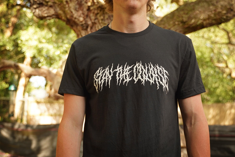 Person wearing a black T-shirt with "Stay the Course" printed in white in heavy metal style