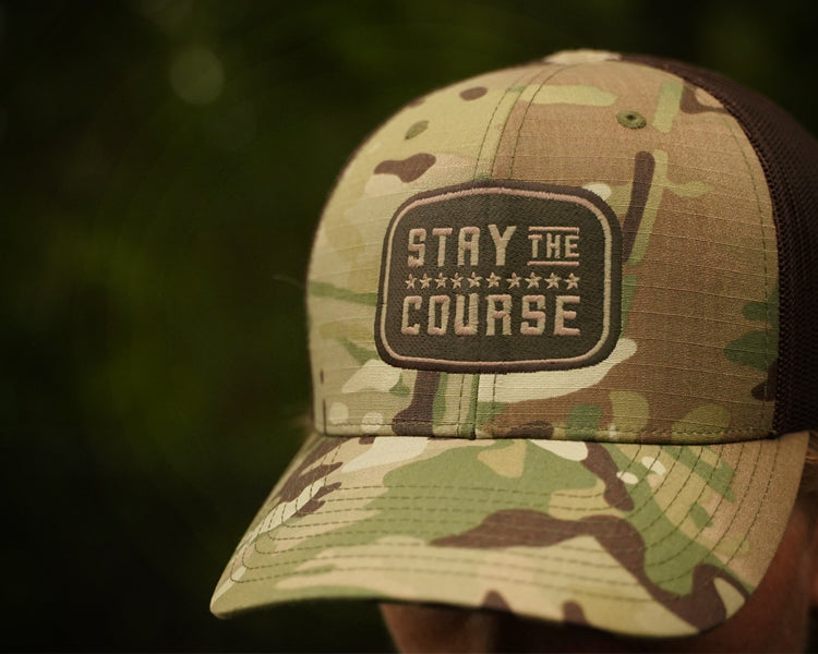 Camouflage cap with 'Stay the Course' patch on a blurred natural background