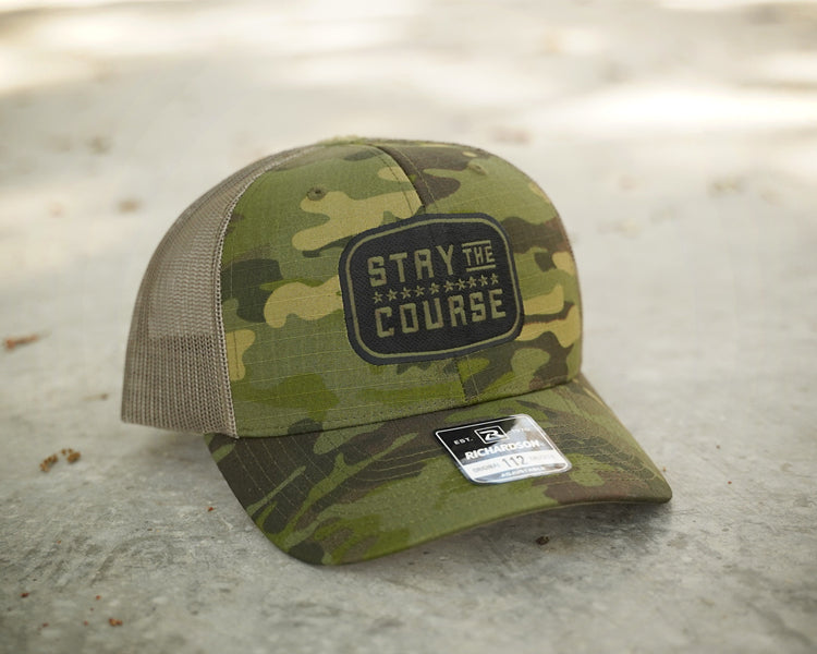 Camouflage cap with 'Stay the Course' patch on a concrete surface