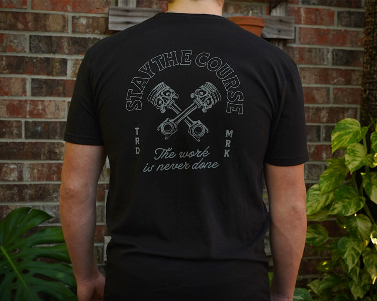 Person wearing a black t-shirt with a motivational quote on the back, standing against a brick wall.