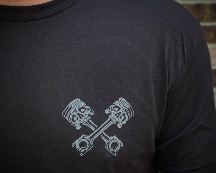 Person wearing a black t-shirt with a gray engine piston design on a brick wall background