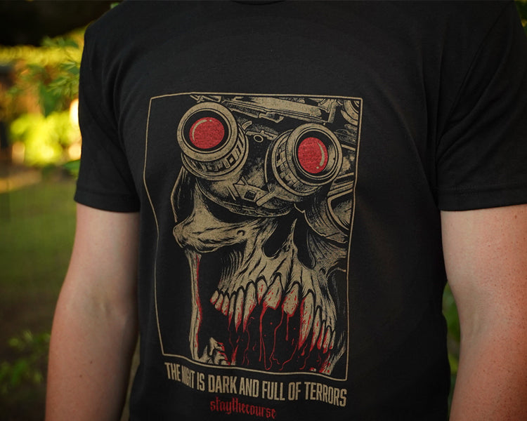 Person wearing a black t-shirt with tan and red graphic print and the words "the night is dark and full of terrors", in an outdoor setting.