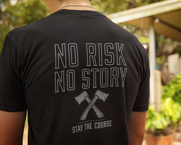 Person wearing a black t-shirt with 'No Risk No Story Stay the Course' text and graphic outdoors.