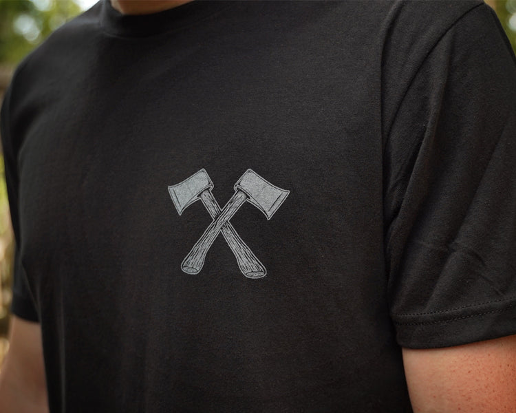 Person wearing a black t-shirt with a graphic of two crossed axes on a blurred outdoor background
