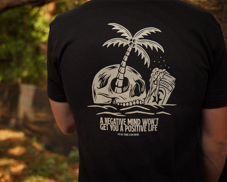 Person wearing a black t-shirt with a skull and palm tree design and text.