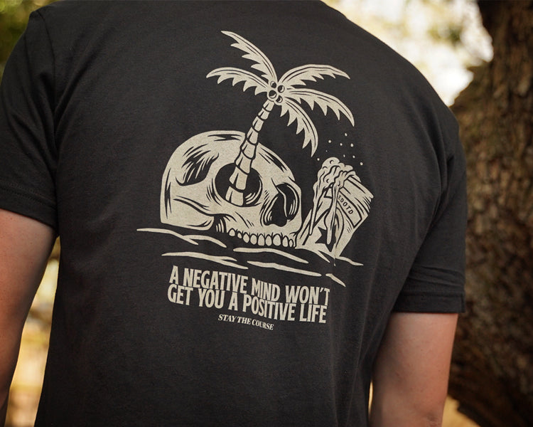 Person wearing a black t-shirt with a skull and palm tree design and motivational quote.