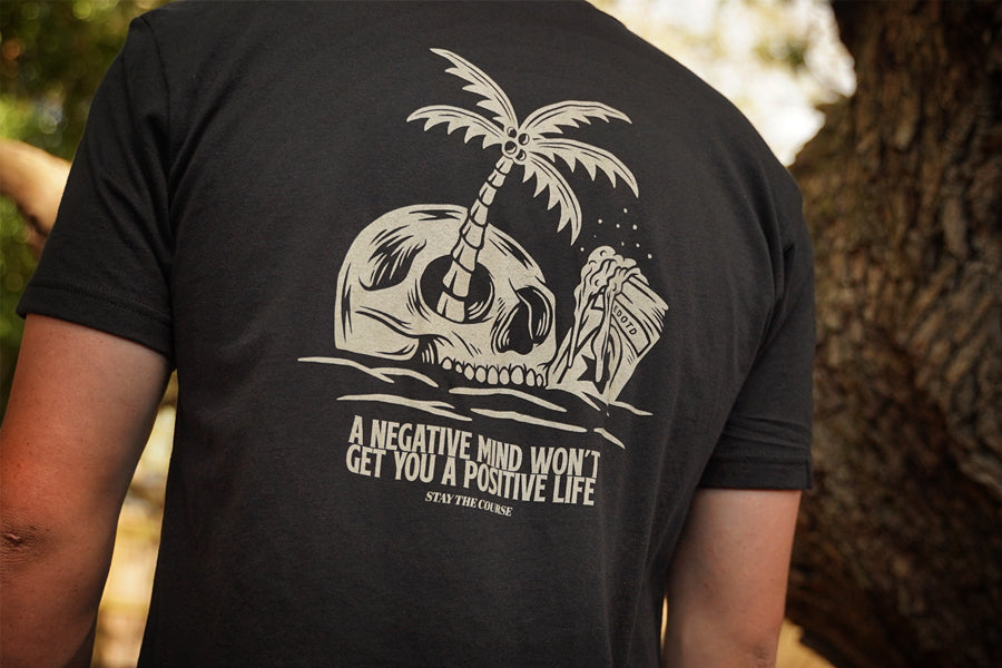 Person wearing a black t-shirt with a skull and palm tree design and motivational quote.