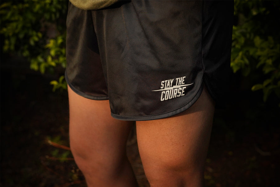 Black athletic shorts with 'Stay the Course' text on a person against a dark background