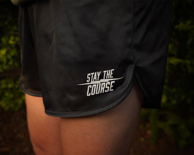 Black shorts with 'Stay the Course' text on a person against a blurred natural background