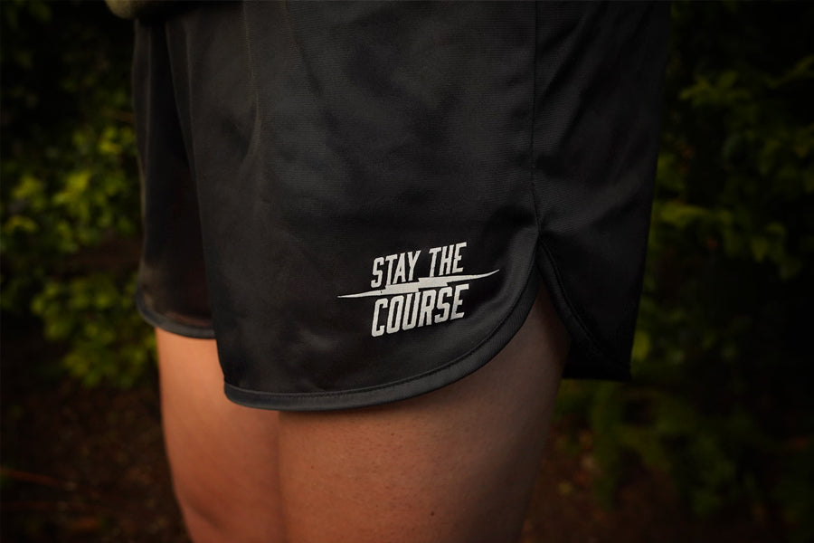 Black shorts with 'Stay the Course' text on a person against a blurred natural background