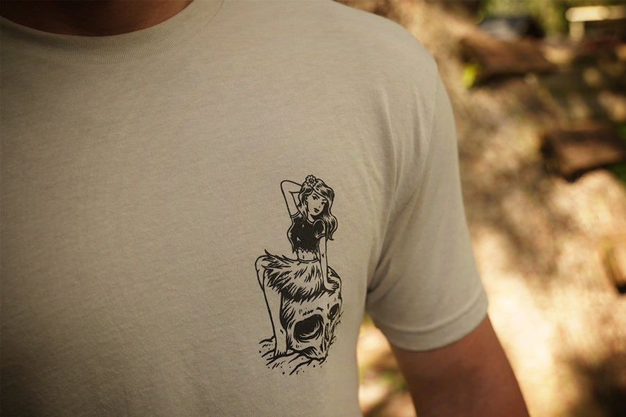 Beige t-shirt with a black graphic design, worn by a person in an outdoor setting.