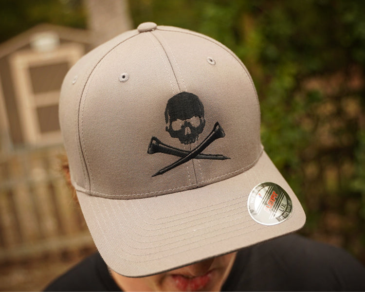 Gray cap with skull and golf tees design worn by a person, blurred background