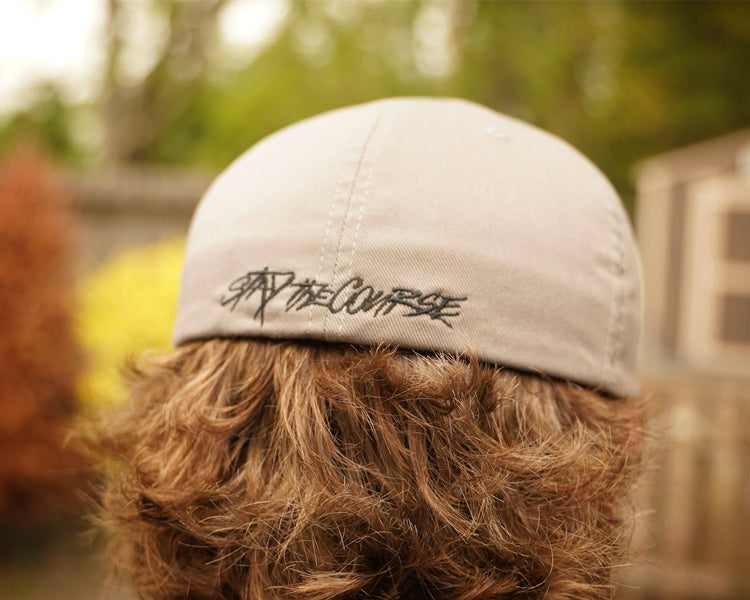 Person wearing a cap with 'By the Course' branding outdoors
