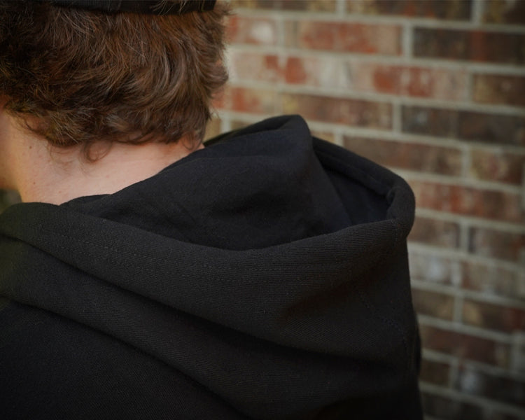 Person wearing a black hoodie with a brick wall in the background