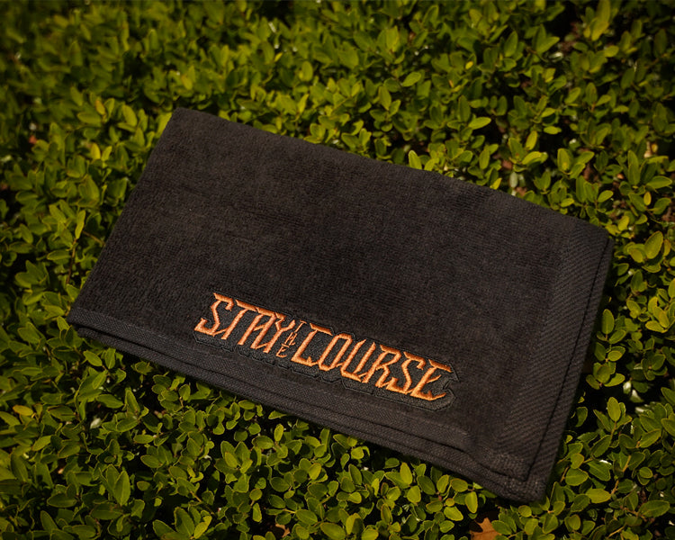 Black towel with 'Stay on the Course' text on grass