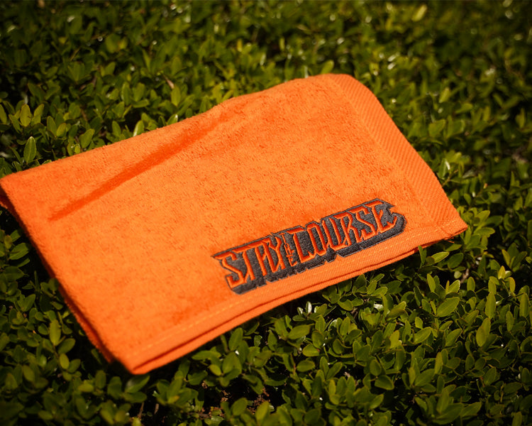 Orange towel with 'Stay the Course' logo on grass