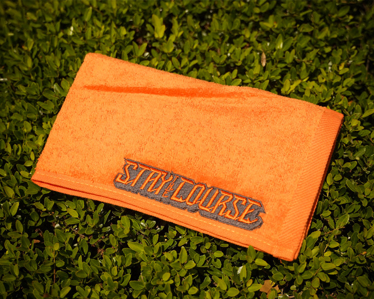 Orange towel with 'STAY the COURSE' branding on grass