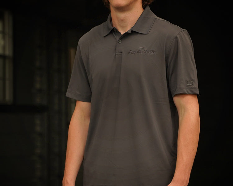 Person wearing a dark gray polo shirt with brand logos on a black background