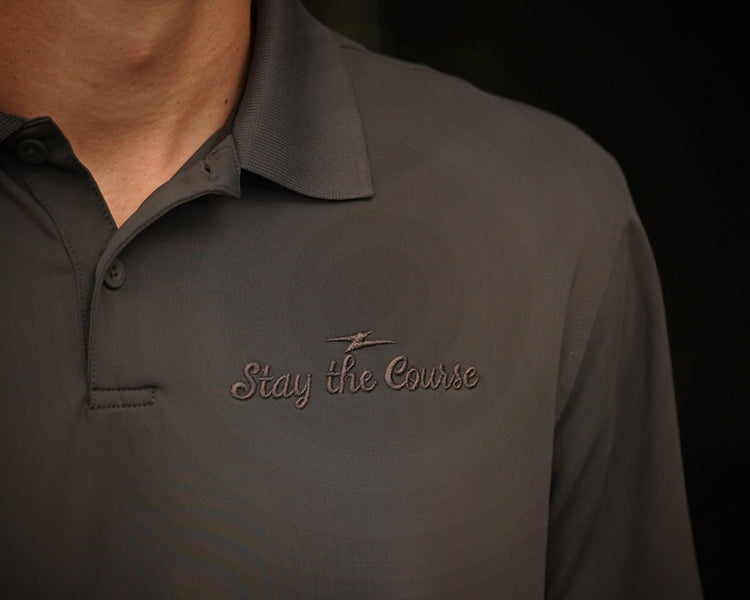Dark gray polo shirt with 'Stay the Course' embroidery on a black background
