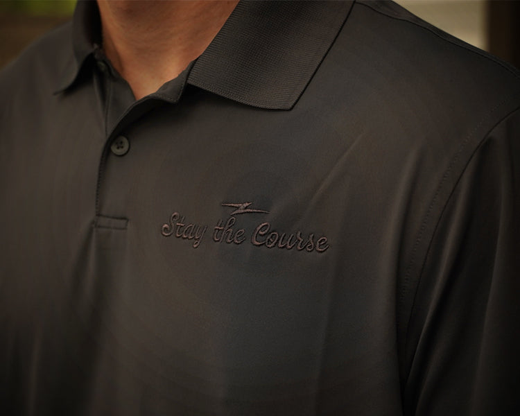 Dark polo shirt with 'Stay the Course' text on a blurred background