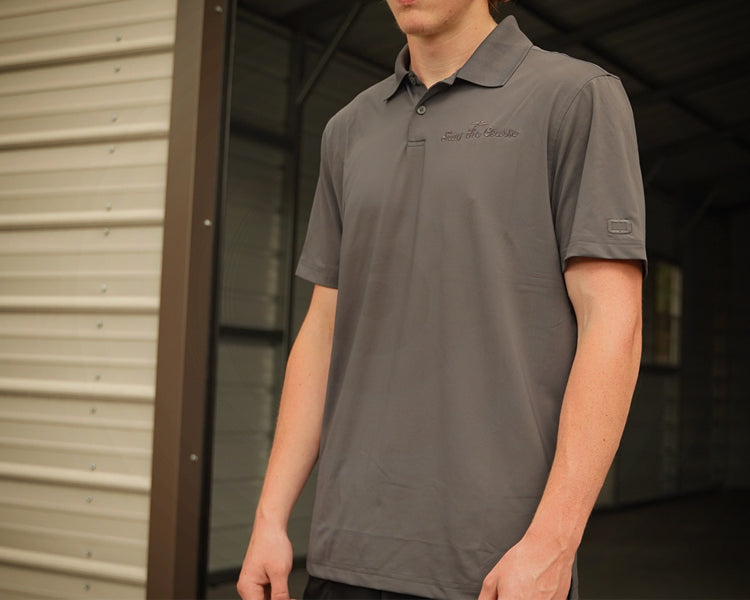 Person wearing a gray polo shirt with a brand logo, standing in front of a metal building