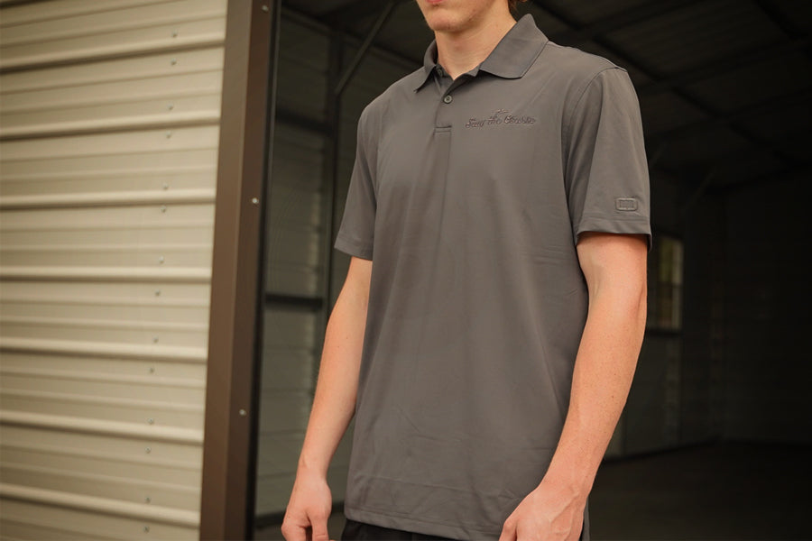 Person wearing a gray polo shirt with a brand logo, standing in front of a metal building