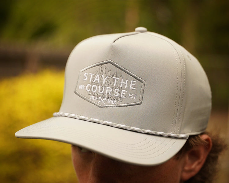 Gray cap with 'Stay the Course' logo worn by a person outdoors