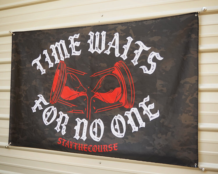 5x3 black camo flag with white and red design that says ice waits for no one, hanging on a metal siding building