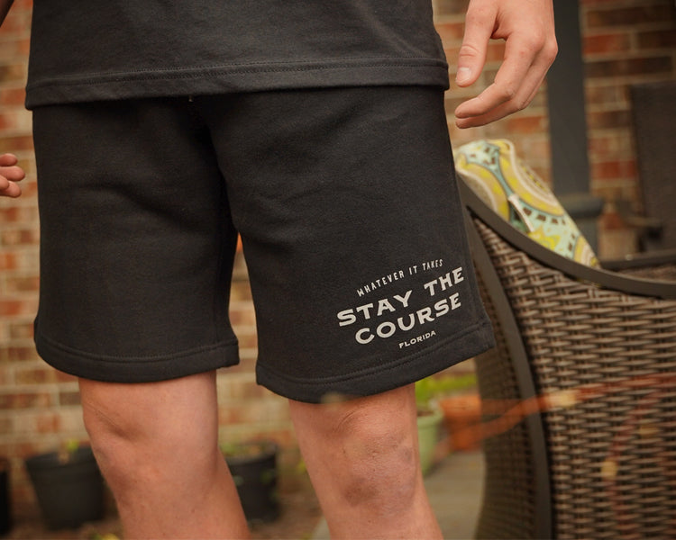 Person wearing black shorts with 'Stay the Course' text, standing outdoors.
