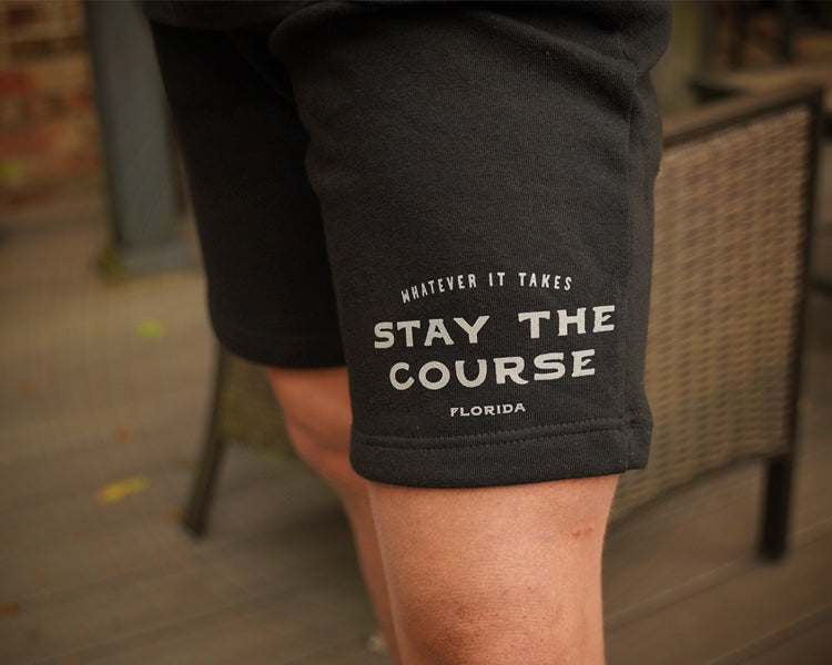 Black shorts with 'Stay the Course Florida' text on a blurred outdoor background