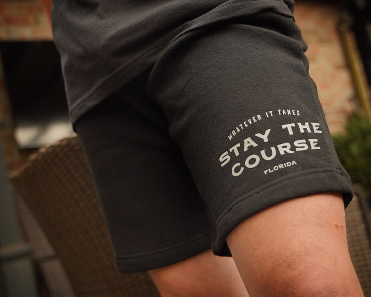 Person wearing black shorts with 'Whatever it takes - Stay the Course' text, blurred background