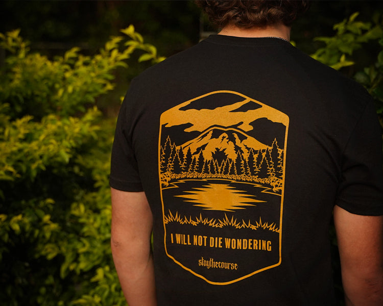 Person wearing a black t-shirt with a golden yellow nature-themed design and text.