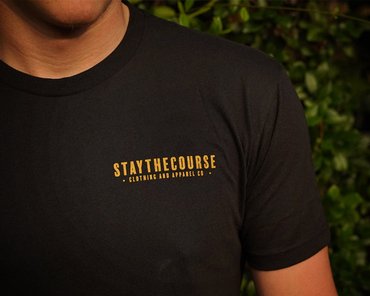 Person wearing a black t-shirt with 'STAYTHECOURSE' logo in gold.