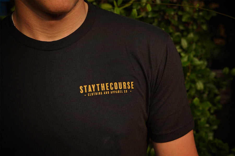 Person wearing a black t-shirt with 'STAYTHECOURSE' logo in gold.