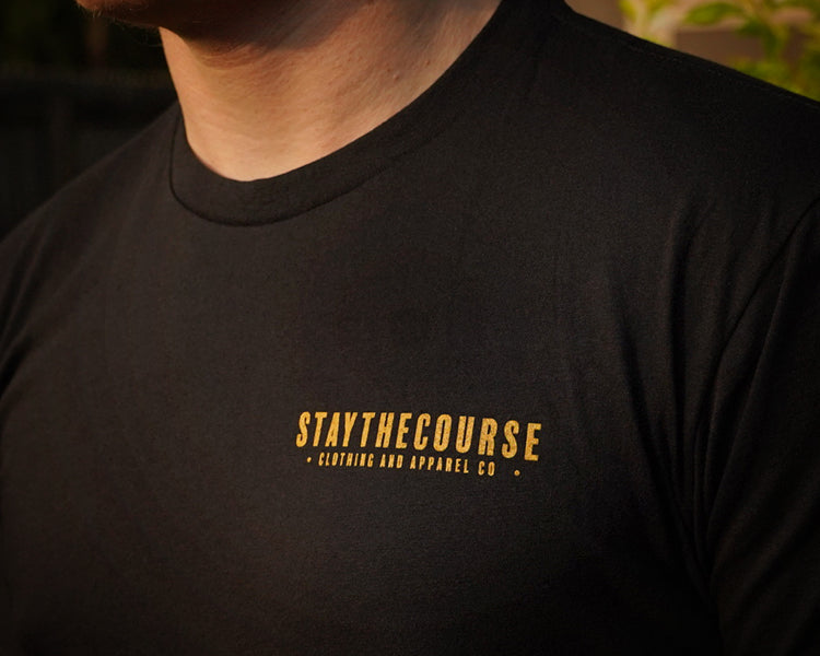 Black t-shirt with 'STAYTHECOURSE' logo on a blurred background