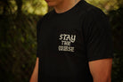 A person wearing a black t-shirt with white graphic that says STAY THE COURSE, standing against a blurred background