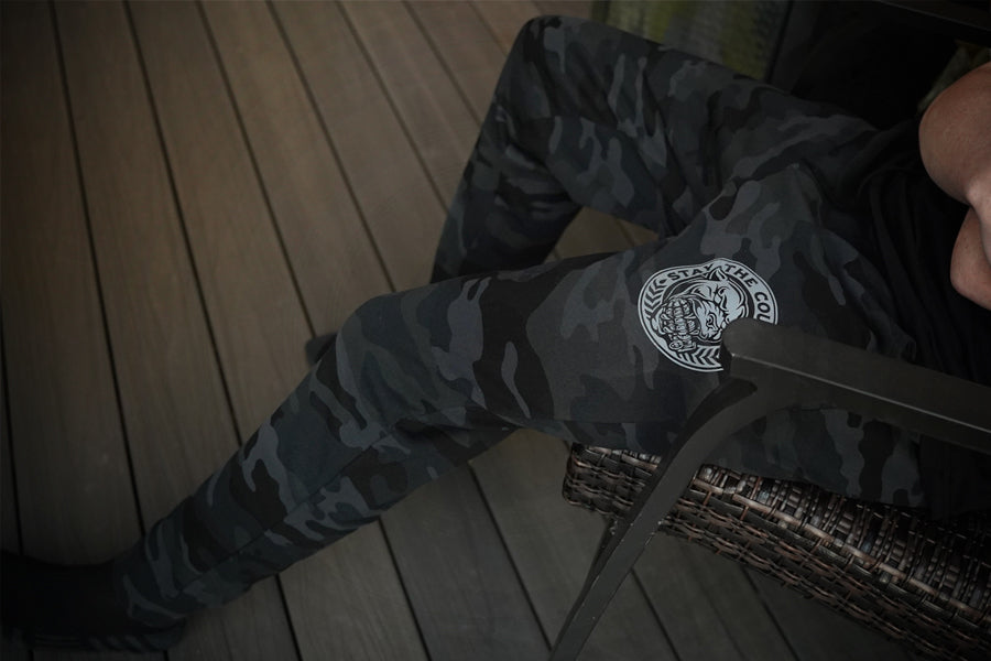 Person wearing camouflage pants with a logo on a wooden floor