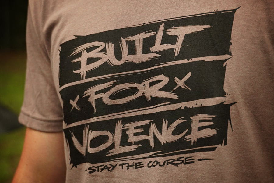 T-shirt with 'Built for Violence, Stay the Course' text on a blurred background