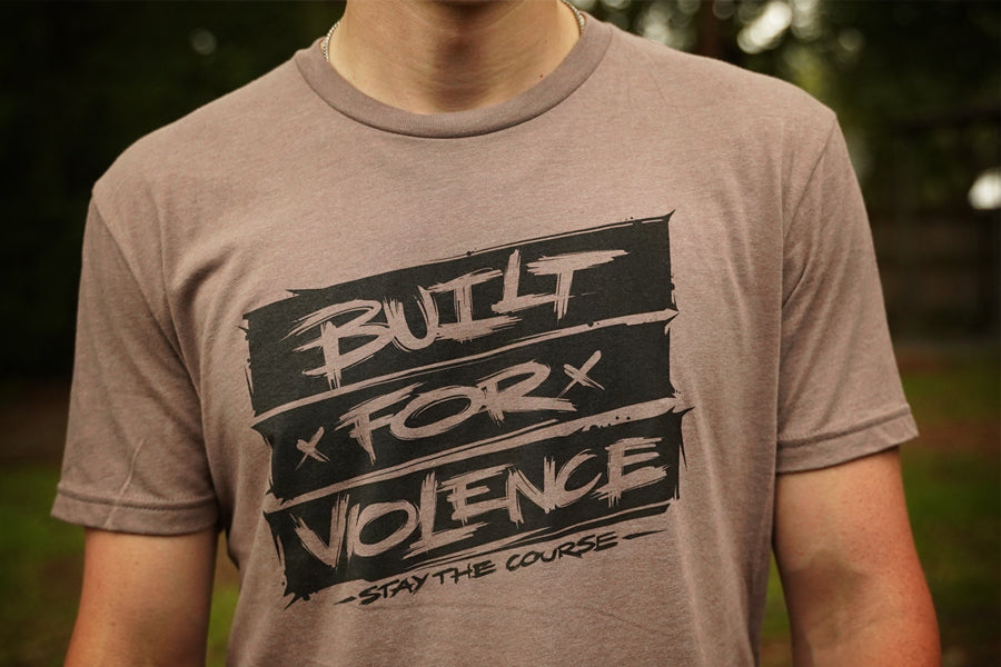 Person wearing a brown t-shirt with 'Built for Violence' graphic design.