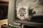 Camouflage-style 'Stay the Course' decal on a vehicle window with a blurred outdoor background.