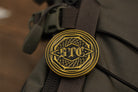 Close-up of a brass emblem with 'STC' on a brown bag.
