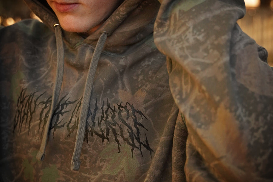 Person wearing a hoodie with a dark logo design on a neutral background