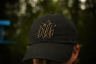 Black cap with STC black and gold logo worn by a person, blurred background