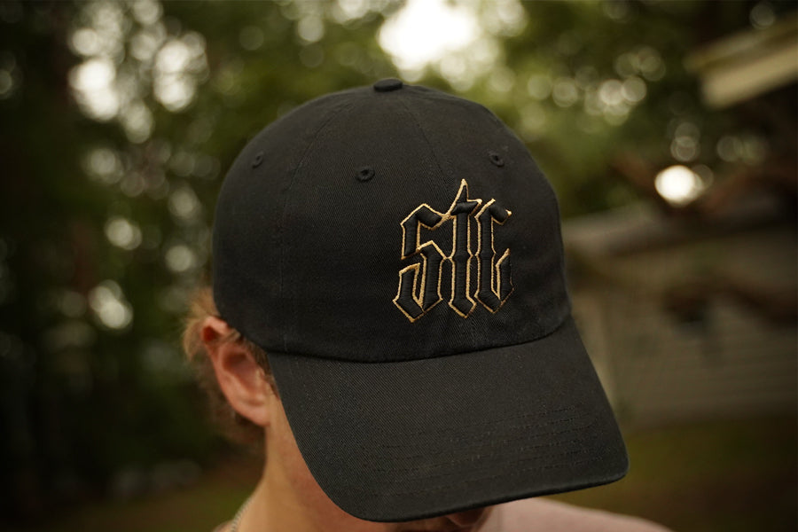 Black cap with gold logo worn by a person outdoors
