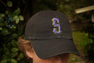 Person wearing a black cap with a purple and green logo outdoors