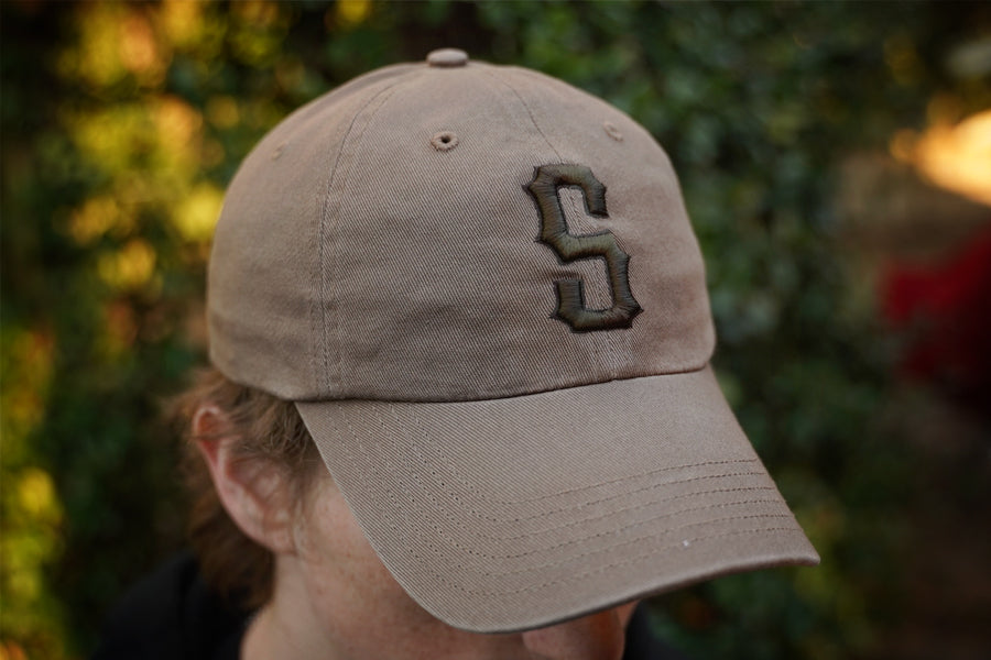 Beige cap with a logo worn by a person against a blurred natural background