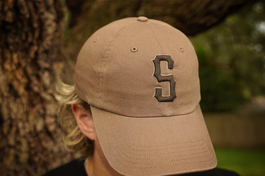 Tan baseball cap with a large 'S' logo worn by a person, blurred background